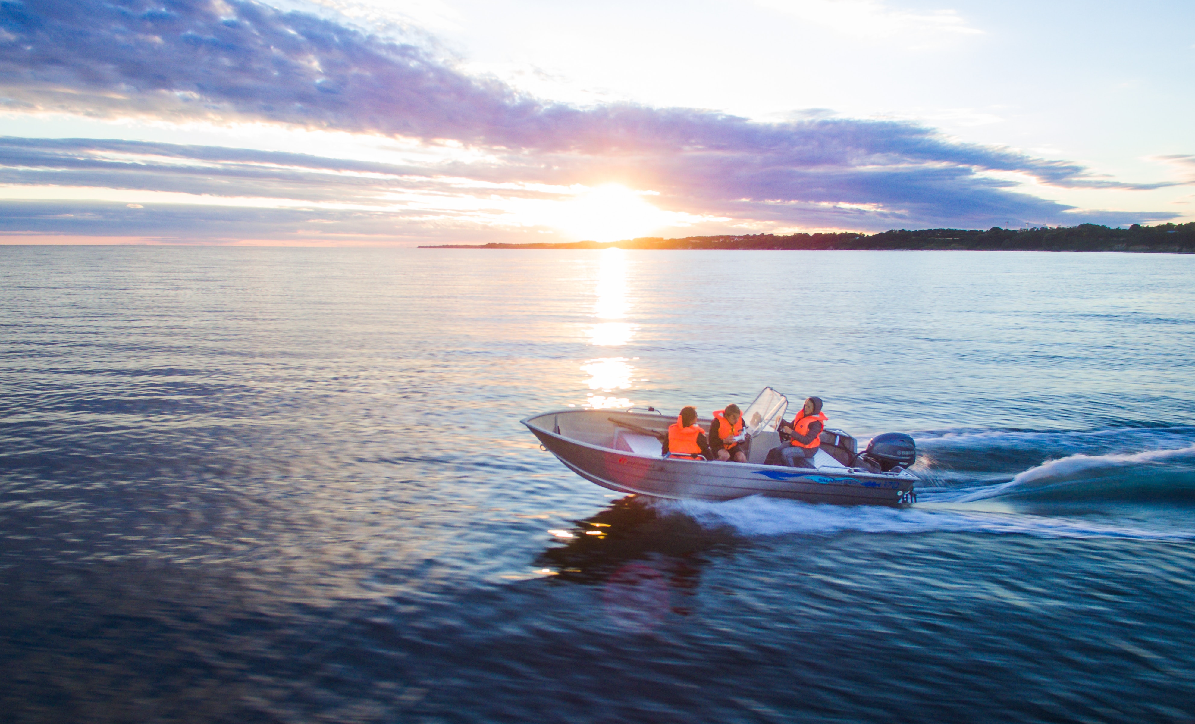 Small boat on the water with three people on board in life jackets at sunset.