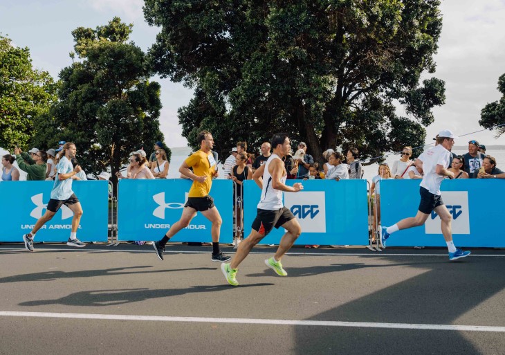Four participants shown from the side running along the road in Round the Bays.