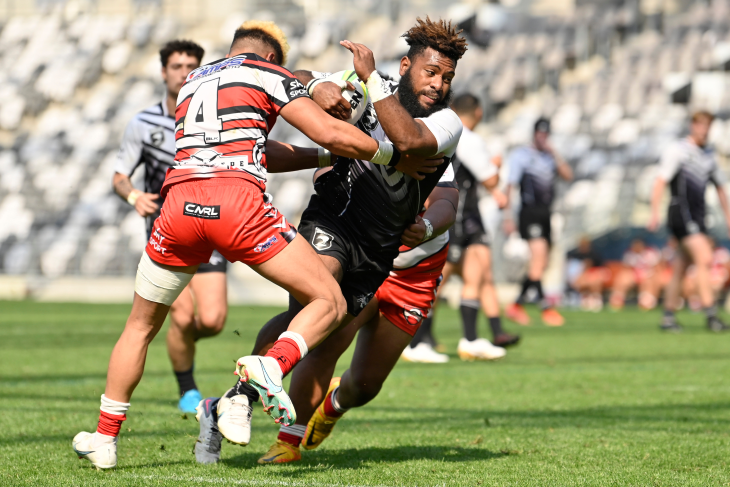 A male rugby league player running with the ball and being tackled.