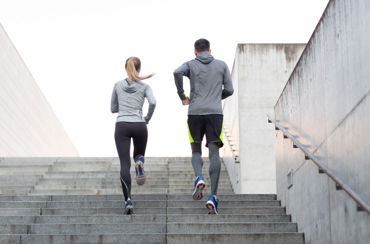 A man and a woman shown from behind running up concrete stairs.