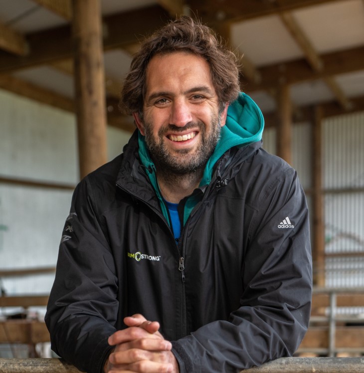Sam Whitelock leaning on a fence on a farm and smiling. 