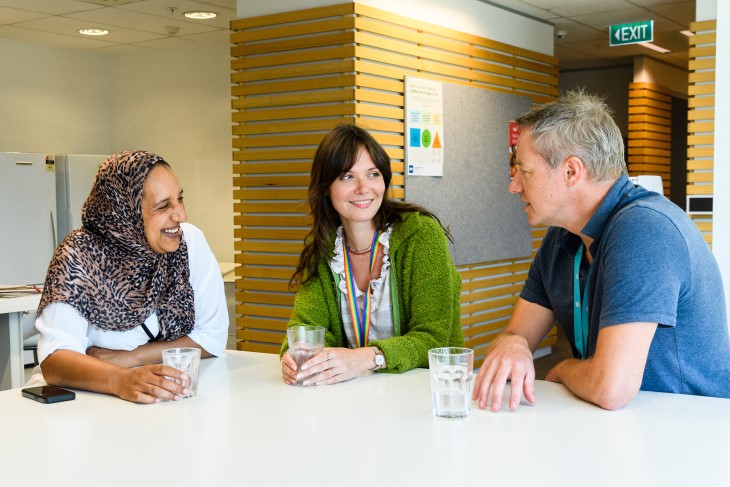 Three ACC staff members sitting at a table and talking to each other. 