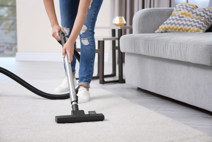 A person using a vacuum to clean their living room rug. 