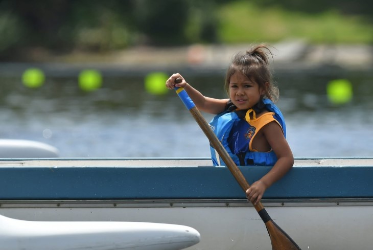 A young girl paddling in a waka ama canoe.