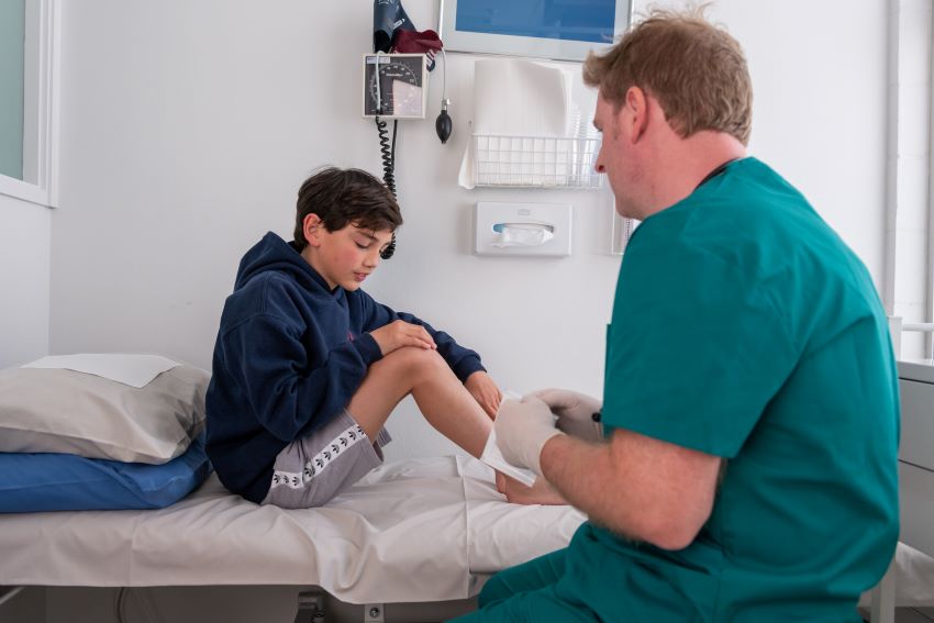 Health provider treating young patient with leg injury on medical bed